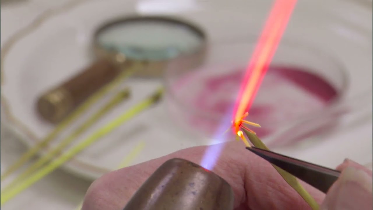Glass rods held to a torch flame with tweezers, making them malleable for glassworking. This process is also called torchworking or lampworking.