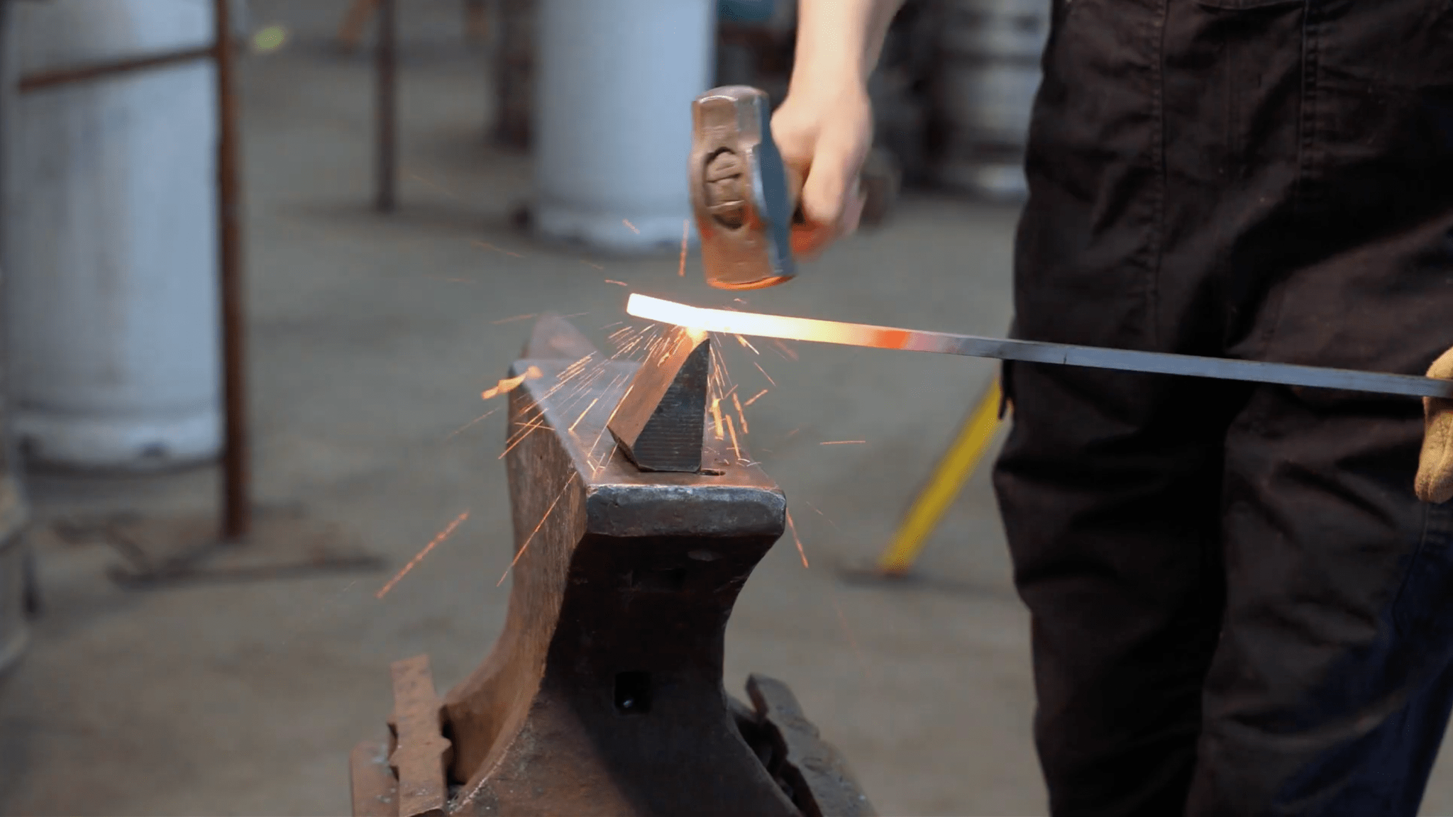 Blacksmith Heather McLarty hammering white-hot, forged steel against hot cutter chisel in the hardy hole of an anvil at Adam's Forge in Los Angeles, California.