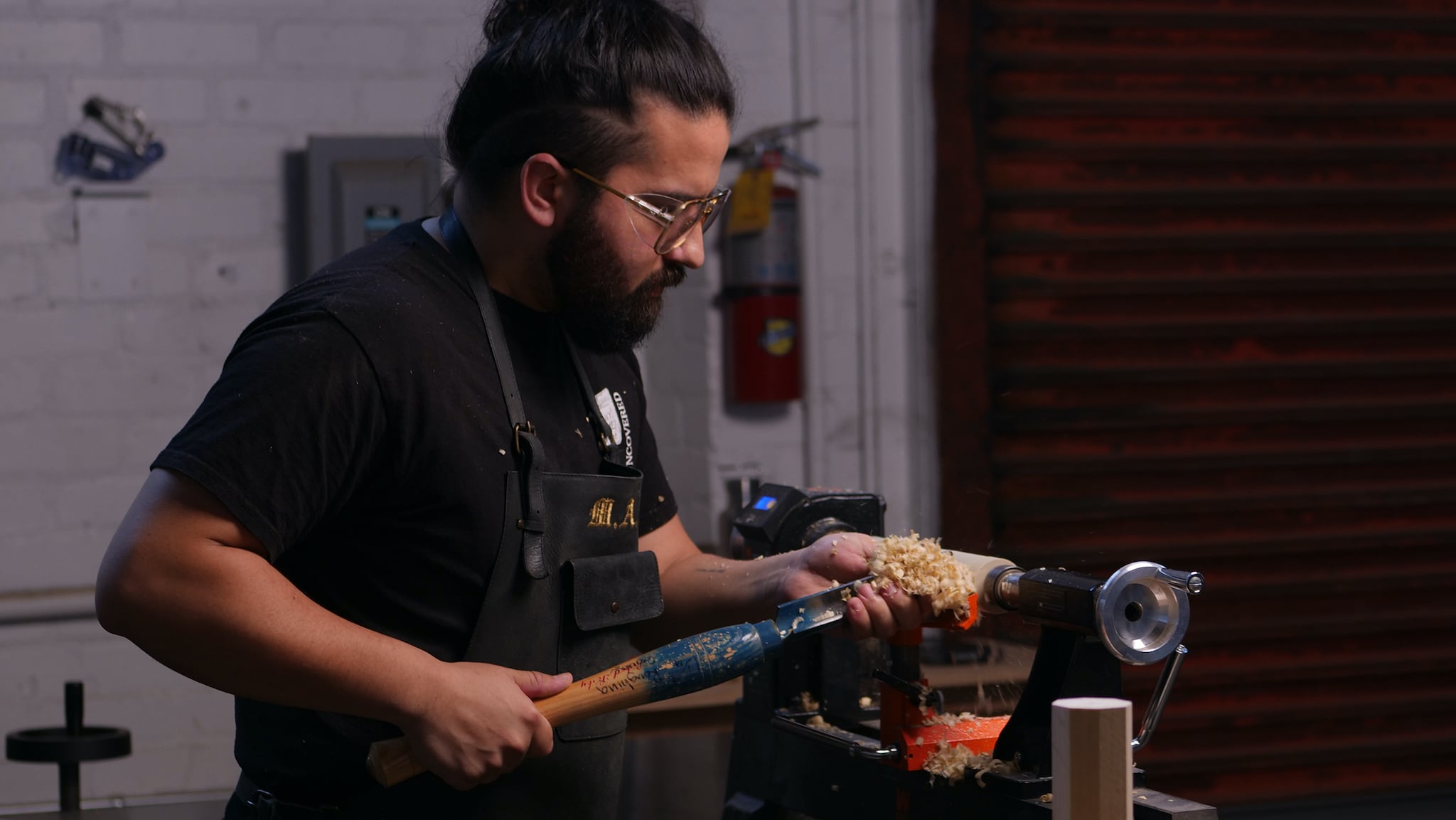 Turning poplar spindle with gouge and push stick creating wood shavings at Allied Woodshop in Los Angeles, California